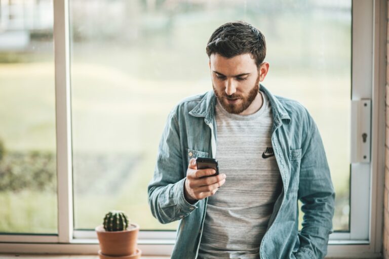 Mężczyzna stojący przy oknie i czekający, patrząc w ekran telefonu
